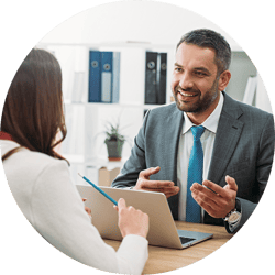 business man smiling and speaking to business woman at his desk